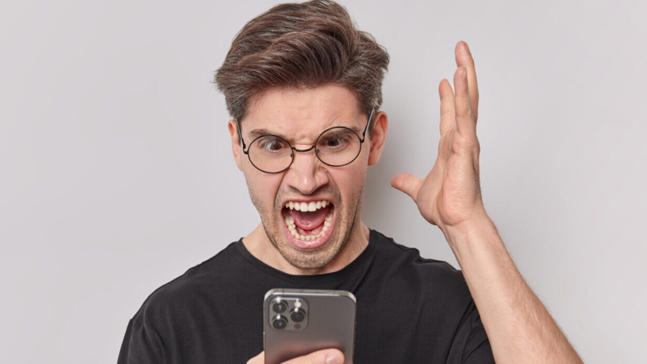 Pissed off annoyed man screams angrily keeps palm raised stares at smartphone being outraged after rough conversation wears round spectacles casual black t shirt isolated over white background