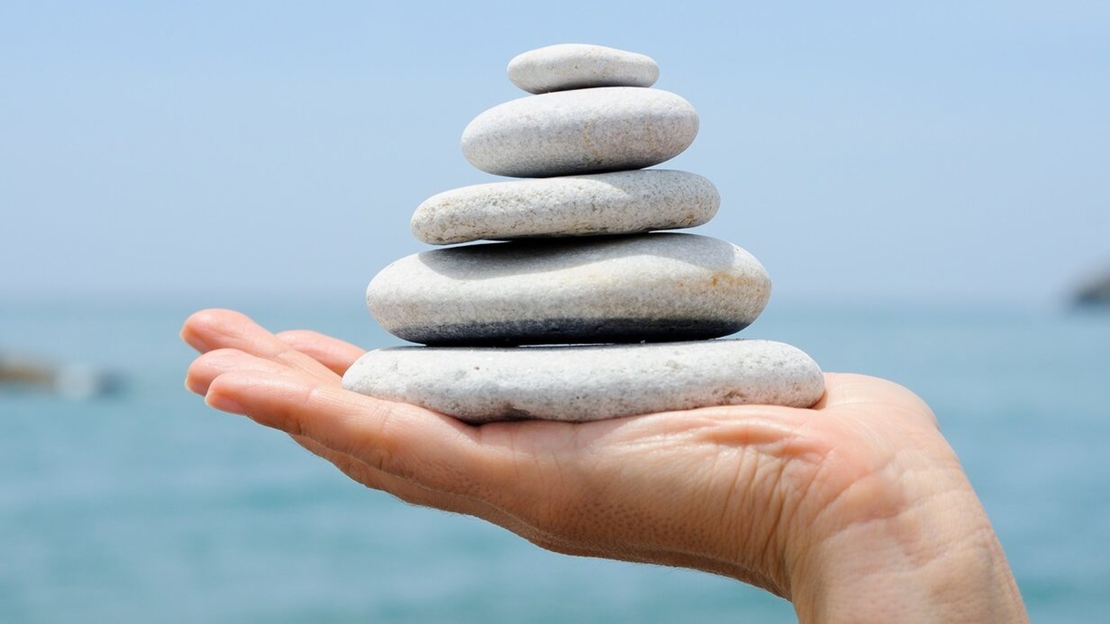 Close-up of gravel pile in woman's hands with sea background